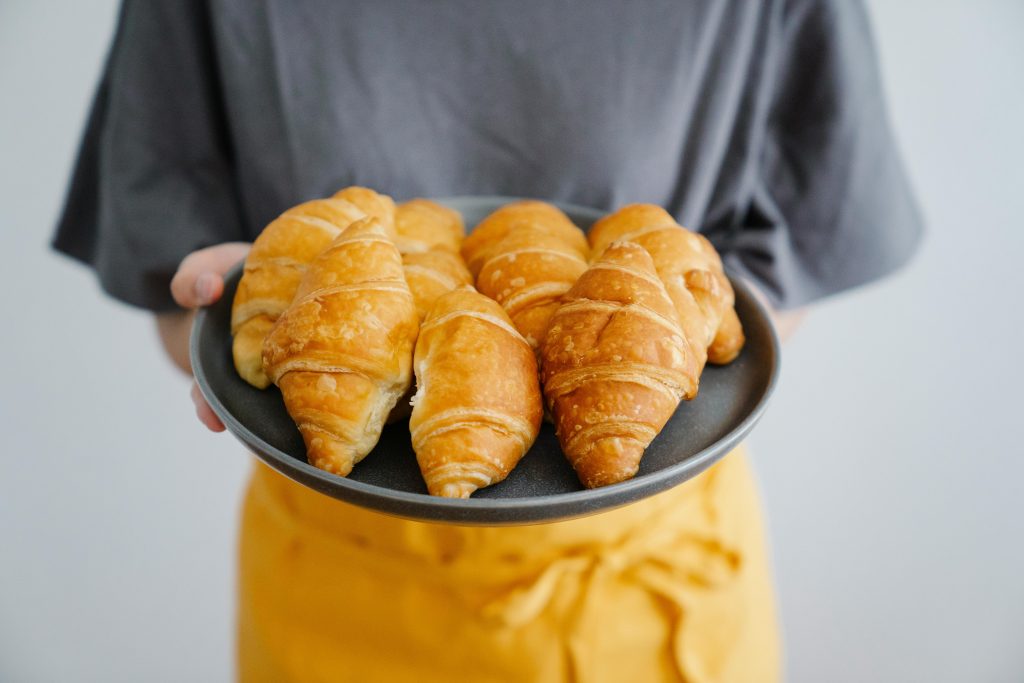 Plate of golden croissants being held by person, showcasing fresh baked goods.